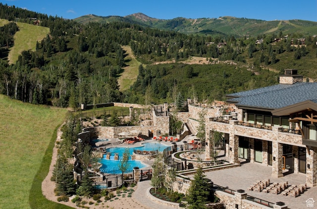 bird's eye view of a mountain backdrop, a forest, and a pool