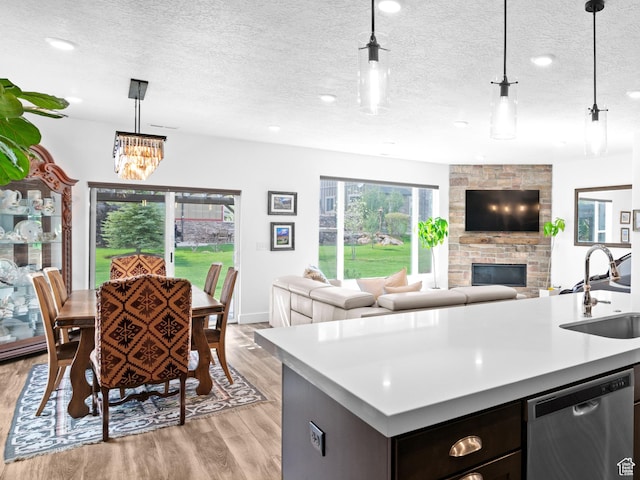 kitchen featuring stainless steel dishwasher, a sink, light countertops, a fireplace, and light wood-style flooring