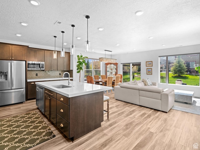 kitchen featuring stainless steel appliances, a sink, light wood-type flooring, a textured ceiling, and light countertops