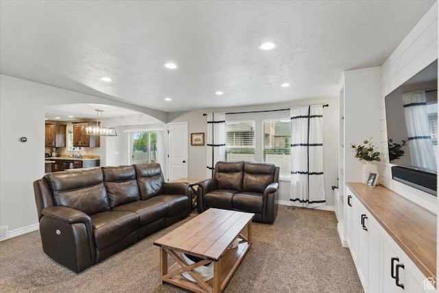 carpeted living room with arched walkways, recessed lighting, baseboards, and a textured ceiling