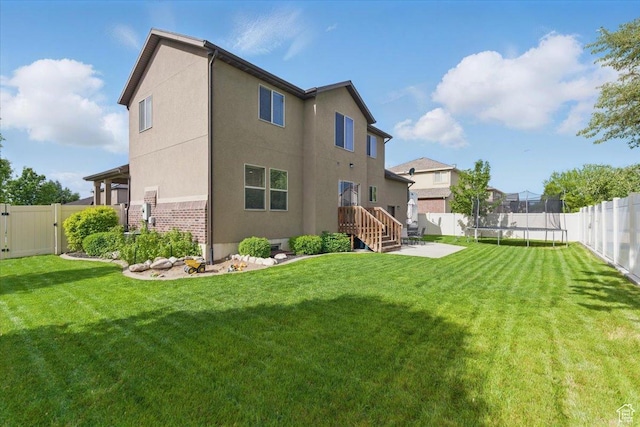 rear view of property with a trampoline, stucco siding, a patio, a gate, and brick siding