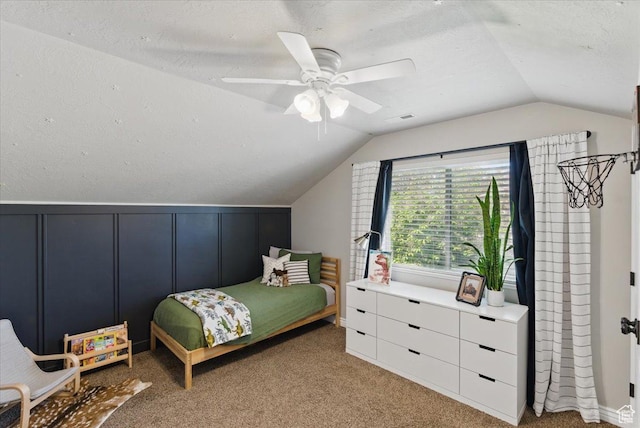 bedroom featuring lofted ceiling, a decorative wall, carpet, and a ceiling fan