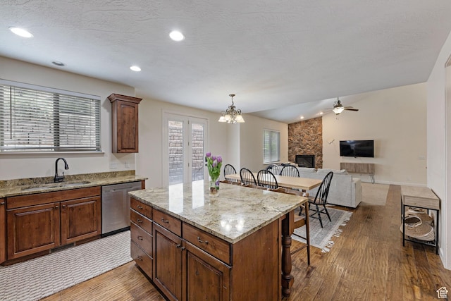 kitchen featuring a sink, dishwasher, wood finished floors, a breakfast bar area, and a large fireplace