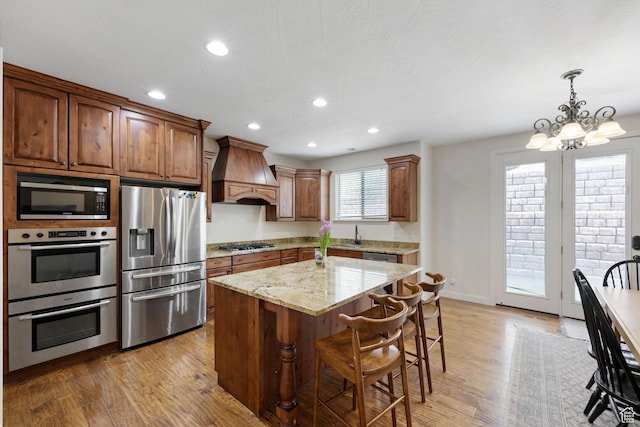 kitchen featuring appliances with stainless steel finishes, premium range hood, light wood finished floors, a chandelier, and recessed lighting