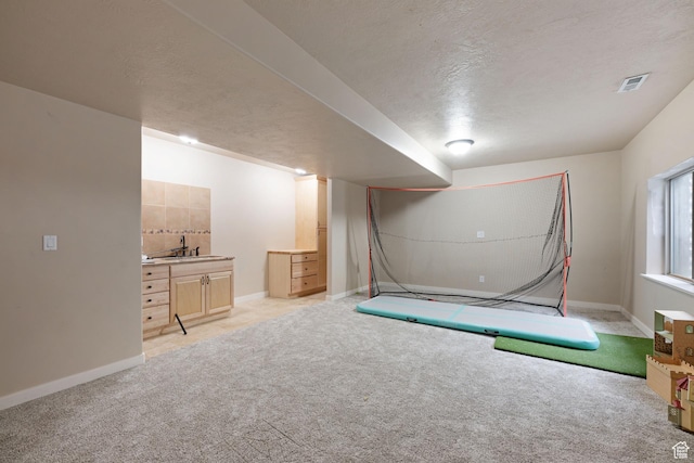 basement featuring a sink, light carpet, baseboards, and a textured ceiling