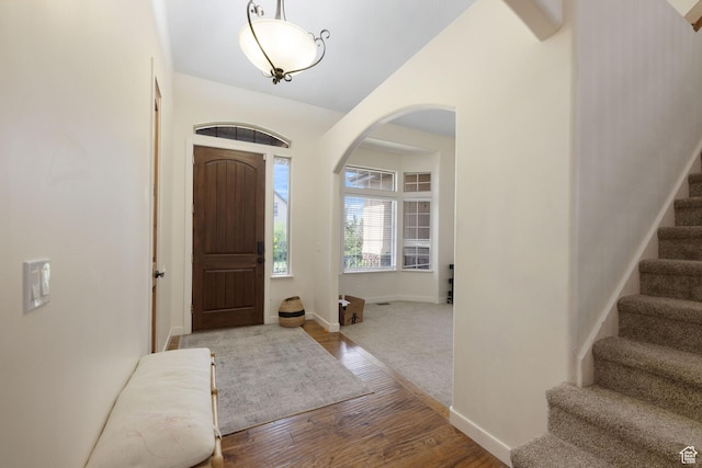 entrance foyer featuring arched walkways, stairs, wood finished floors, and baseboards
