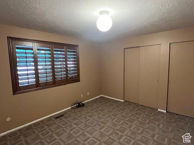 unfurnished bedroom with a textured ceiling, baseboards, and multiple closets