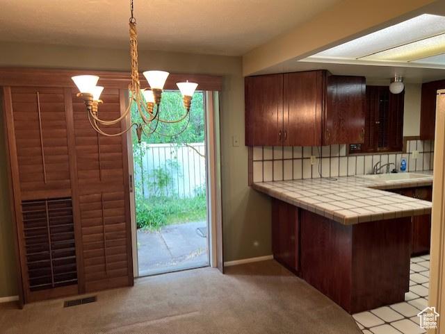 kitchen with tile counters, a chandelier, light carpet, and backsplash