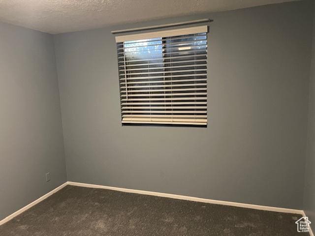 spare room with dark colored carpet, baseboards, and a textured ceiling