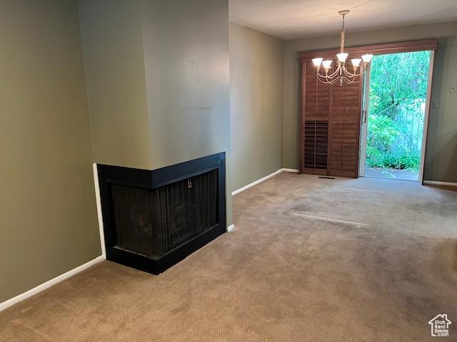 unfurnished living room featuring carpet floors, a chandelier, and baseboards