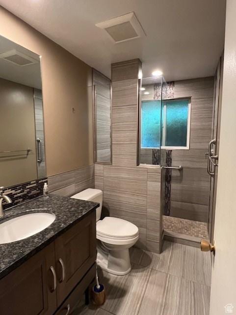 full bath featuring tile walls, a shower stall, toilet, vanity, and tile patterned flooring