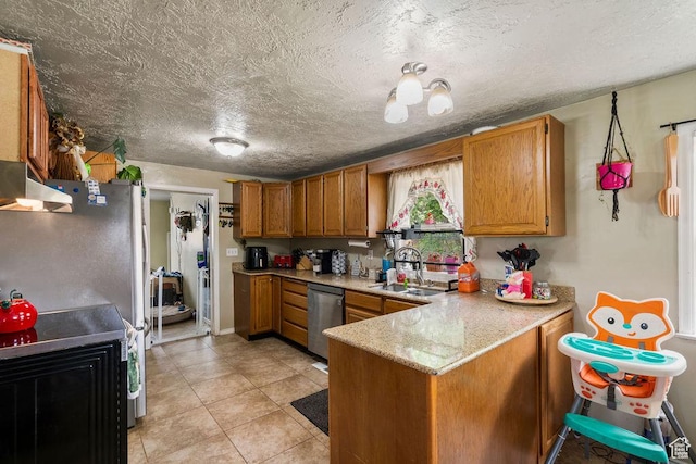 kitchen with appliances with stainless steel finishes, a sink, a peninsula, brown cabinets, and a textured ceiling