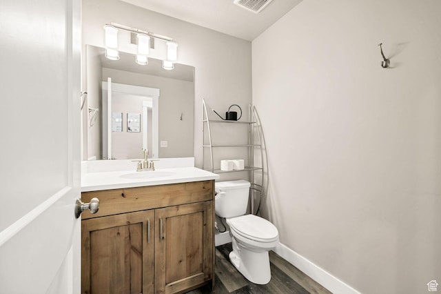 half bathroom featuring toilet, vanity, wood finished floors, and baseboards