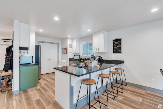 kitchen with a peninsula, a kitchen breakfast bar, light wood finished floors, white cabinets, and recessed lighting