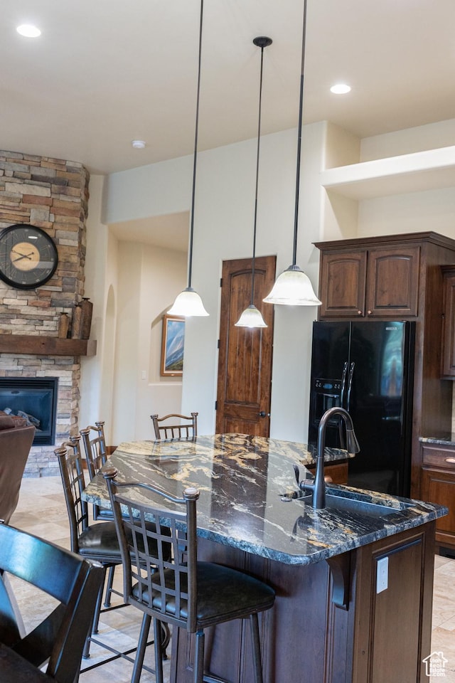 2090 N Tuweap Dr Unit 15, St George, UT 84770 - kitchen featuring black fridge, a fireplace, an island with sink, dark stone countertops, and a sink