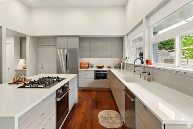 kitchen with stainless steel appliances, modern cabinets, a sink, gray cabinetry, and dark wood finished floors
