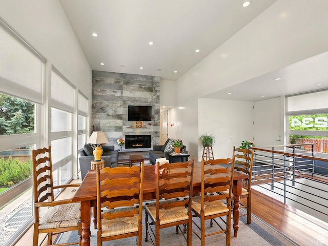 dining space with recessed lighting, wood finished floors, a fireplace, and a towering ceiling