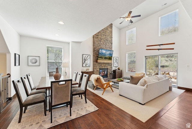 dining room featuring dark wood-type flooring, ceiling fan, a fireplace, baseboards, and high vaulted ceiling
