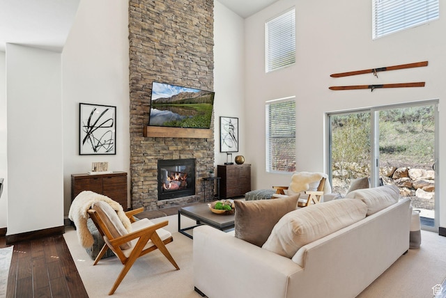 living area with a fireplace, a towering ceiling, hardwood / wood-style flooring, and baseboards