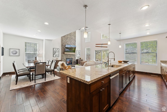 kitchen featuring a sink, stainless steel dishwasher, baseboards, a fireplace, and dark wood-style floors