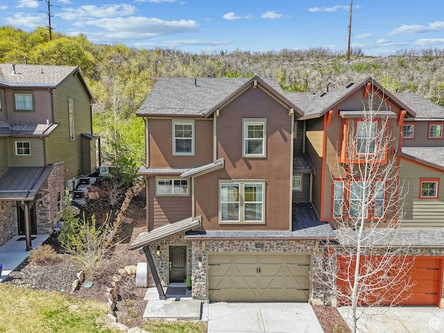 multi unit property featuring an attached garage, stone siding, driveway, and stucco siding