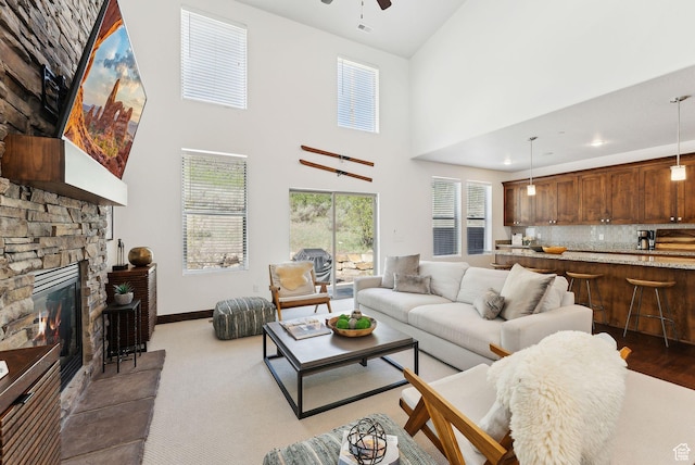 living room featuring ceiling fan, a high ceiling, baseboards, and a fireplace