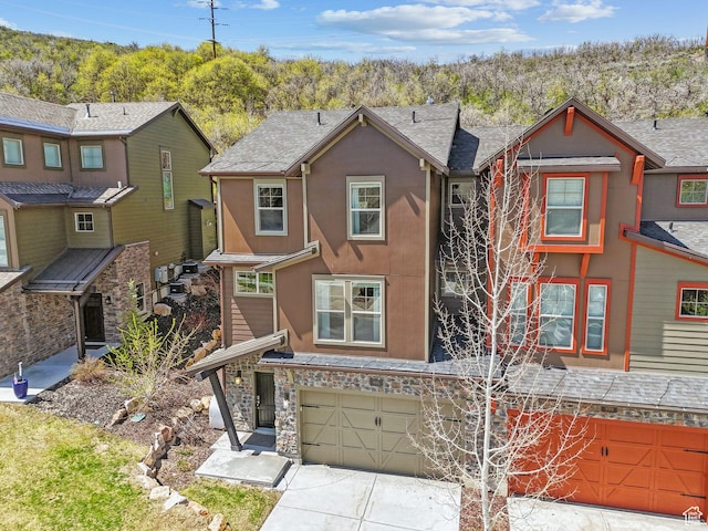 multi unit property with a garage, concrete driveway, stucco siding, and stone siding