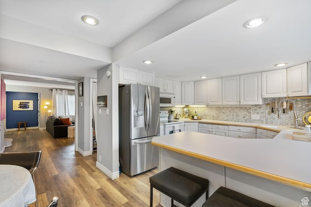 kitchen featuring white appliances, baseboards, a peninsula, tasteful backsplash, and recessed lighting