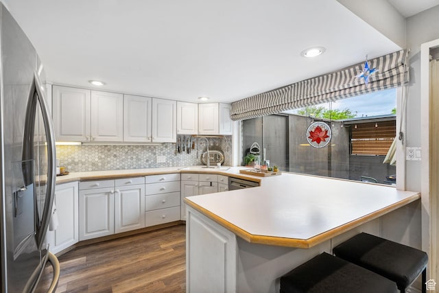 kitchen with stainless steel fridge with ice dispenser, a peninsula, dark wood finished floors, white cabinets, and light countertops