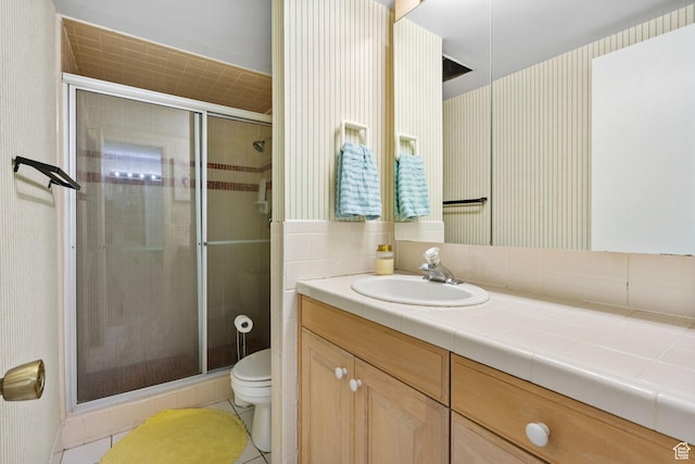 bathroom with toilet, a shower stall, vanity, wallpapered walls, and tile patterned flooring