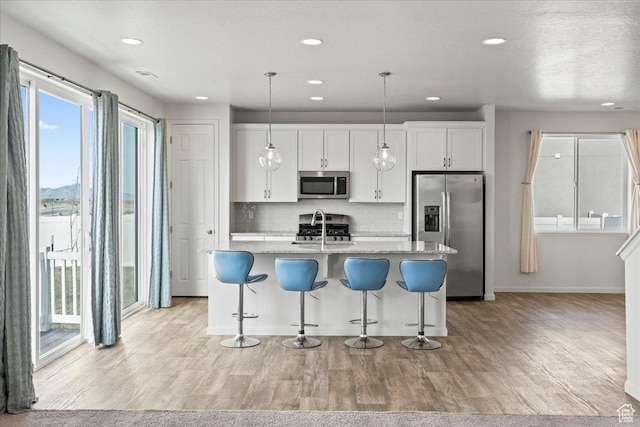 6405 N Appaloosa Dr, Stansbury Park, UT 84074 - kitchen featuring appliances with stainless steel finishes, an island with sink, backsplash, light wood-type flooring, and a kitchen bar