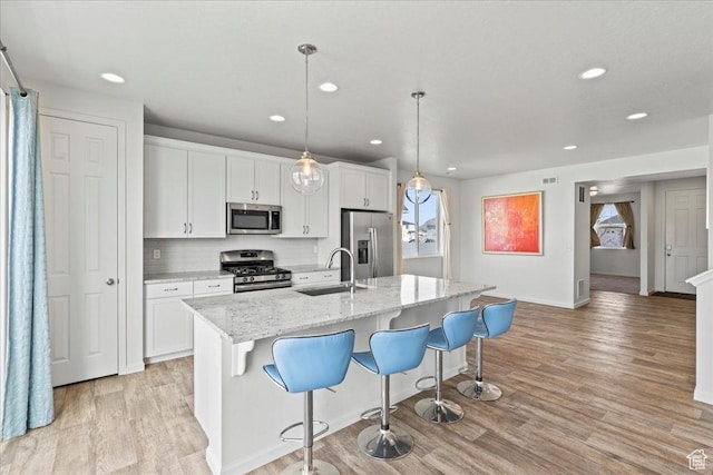 6405 N Appaloosa Dr, Stansbury Park, UT 84074 - kitchen with stainless steel appliances, a sink, light wood-style floors, recessed lighting, and a kitchen island with sink