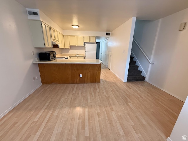 136 E 400 N Unit 108, Provo, UT 84606 - kitchen with freestanding refrigerator, a peninsula, under cabinet range hood, light countertops, and light wood-style floors