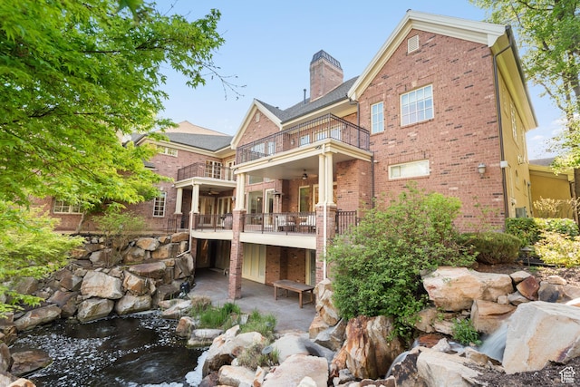 rear view of property with a balcony, brick siding, ceiling fan, a chimney, and a small pond