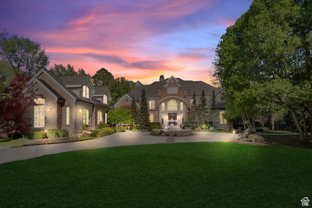 french country home with a front yard, stone siding, and curved driveway
