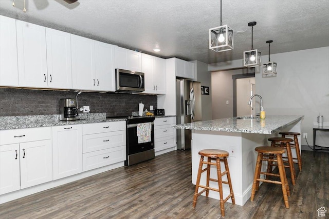 kitchen with appliances with stainless steel finishes, a sink, dark wood-style flooring, decorative backsplash, and white cabinetry