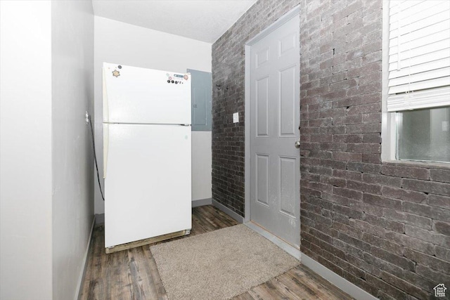 kitchen with freestanding refrigerator, baseboards, wood finished floors, brick wall, and electric panel