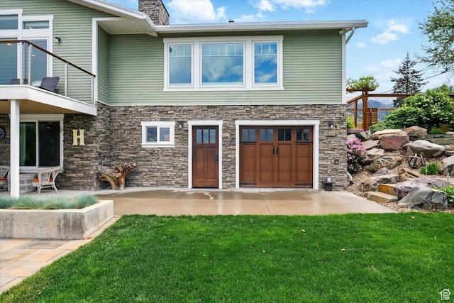 rear view of house featuring stone siding, a chimney, a lawn, and an attached garage