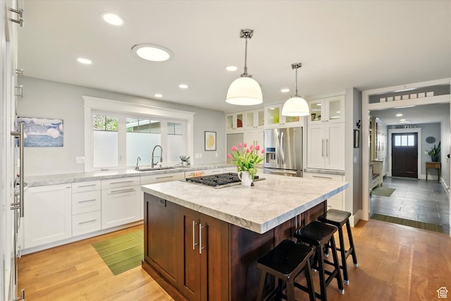 kitchen with stainless steel appliances, a kitchen island, a sink, a kitchen breakfast bar, and white cabinets