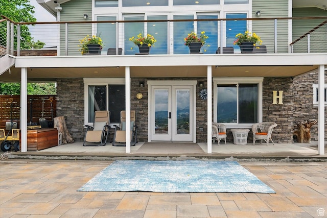 rear view of property featuring french doors, stone siding, a balcony, and a patio