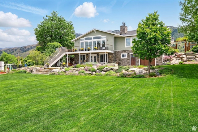 back of property with stone siding, stairway, a deck with mountain view, and a yard