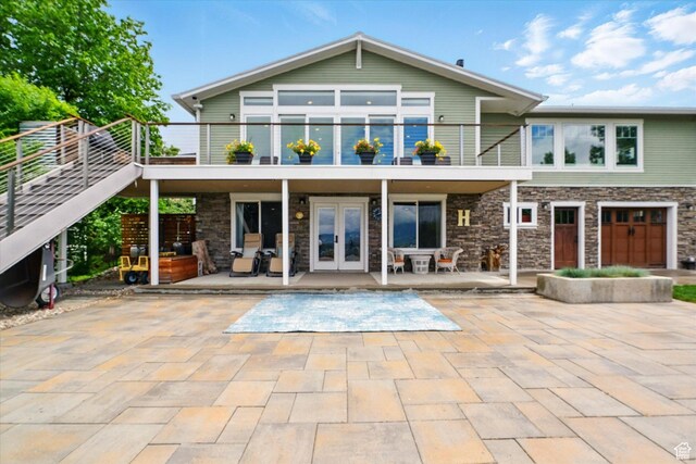 rear view of property featuring french doors, a balcony, stone siding, and a patio area