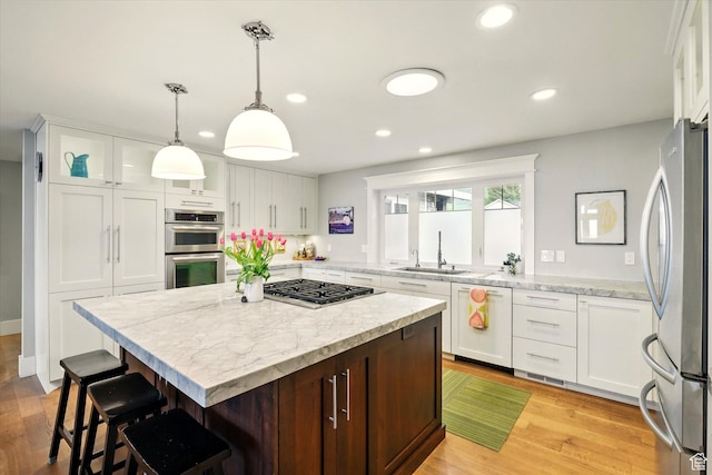 kitchen featuring appliances with stainless steel finishes, a sink, a breakfast bar area, white cabinetry, and recessed lighting