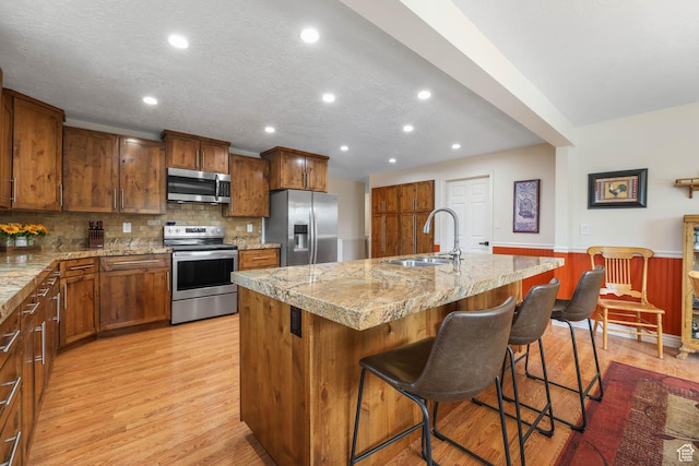 kitchen with appliances with stainless steel finishes, a sink, recessed lighting, light wood finished floors, and a kitchen bar