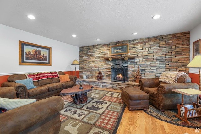 living room with wood finished floors, recessed lighting, a stone fireplace, a textured ceiling, and a wainscoted wall
