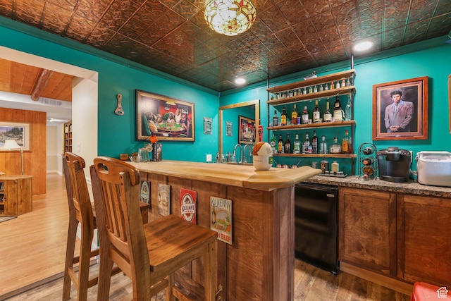indoor wet bar with an ornate ceiling, wood finished floors, fridge, and crown molding