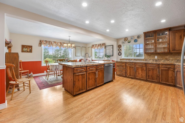 kitchen featuring dishwasher, brown cabinets, light wood finished floors, wainscoting, and a textured ceiling