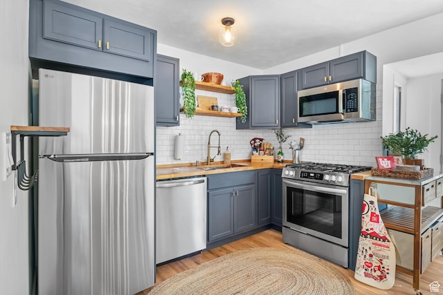 kitchen with appliances with stainless steel finishes, a sink, backsplash, light wood-type flooring, and open shelves
