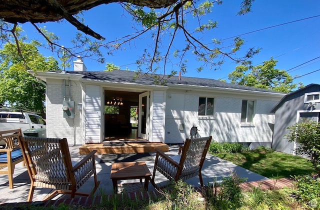 back of house featuring a chimney, brick siding, outdoor lounge area, an outbuilding, and a shingled roof