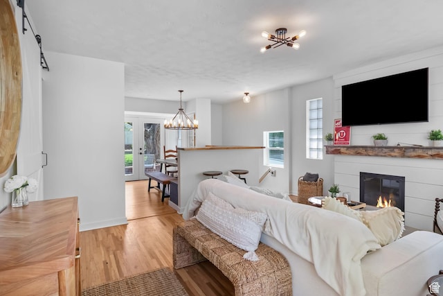 living room with a chandelier, light wood-type flooring, a glass covered fireplace, and baseboards